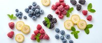 Fresh mixed berries and banana slices with mint leaves arranged on white background. Healthy organic fruit ingredients for smoothies, desserts and snacks.