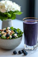 Fresh green salad with blueberries, feta cheese and nuts served with purple smoothie in glass on marble table, white flowers in background for healthy menu.