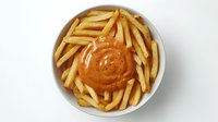 Golden crispy french fries arranged in white ceramic bowl with creamy orange dipping sauce in center, shot from above on white background. Perfect for food service.
