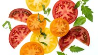 Sliced tomatoes in red, orange, and yellow varieties with fresh green leaves arranged on white background, suitable for food, cooking, and recipe design projects.