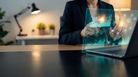 Businesswoman analyzing financial data with holographic charts and graphs on laptop screen in modern office workspace.