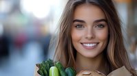 Young woman with radiant smile holding eco-friendly shopping bag with fresh vegetables and bread, representing healthy lifestyle and sustainable shopping habits.