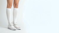 Female legs in white knee-high socks and canvas sneakers on clean background for fashion and lifestyle concepts.