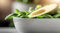 Fresh sliced avocado in white ceramic bowl with green spinach leaves, close-up view on dark background with selective focus and natural lighting.