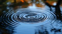 Concentric water ripples creating hypnotic circular pattern on calm water surface with subtle orange reflections from sunset sky, nature abstract background.
