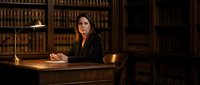Professional female lawyer sitting at wooden desk in traditional law library with legal books for corporate legal services and consultation.