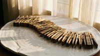 Wooden clothespins arranged in curved line on rustic table near window with natural sunlight creating warm atmosphere for laundry organization concepts.