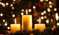 Three burning candles with pine branches against blurred Christmas lights background creating warm festive atmosphere.