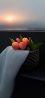 Coral tulips in woven basket with white fabric against sunset backdrop, creating serene mood with soft natural lighting and gentle color palette.