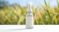 Natural skincare serum bottle with dropper on white surface against blurred green foliage background for organic beauty and wellness product marketing.