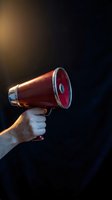 Hand holding red megaphone with dramatic lighting on dark background for communication and announcement concepts.