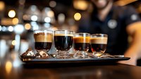Variety of coffee drinks served in glass cups on dark wooden tray with blurred cafe interior background and bokeh lights. Professional barista service.
