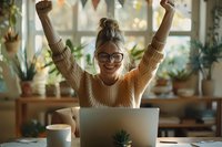 Young woman celebrating success while working from home, raising arms in joy at laptop. Cozy home office setting with houseplants, natural lighting and coffee cup perfect for remote work lifestyle.
