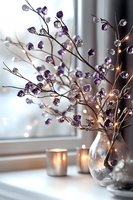 Purple crystal branches in clear glass vase with glowing candles creating cozy atmosphere. Elegant home decor arrangement on windowsill with soft bokeh lights.