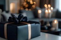 Elegant black gift box with satin bow and gold ribbon on white surface against blurred bokeh lights and candles background, creating luxurious festive atmosphere.