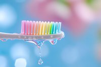 Colorful toothbrush with water drops against soft blue background, macro photography capturing crystal clear droplets and rainbow bristles for dental hygiene concept.