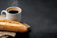Fresh baguette on rustic wooden board with steaming hot black coffee in white ceramic cup against dark background, copy space for menu or text.
