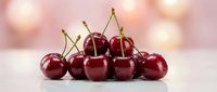 Fresh ripe red cherries with green stems arranged on white surface against soft pink bokeh background for healthy eating and summer fruit concepts.