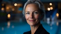 Confident mature businesswoman with elegant silver hair smiling warmly against blurred evening background with bokeh lights, wearing black blazer.
