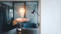 Businessman holding glowing light bulb hologram, symbolizing innovation, creativity, and smart business solutions in a modern office.