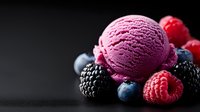 Pink berry ice cream scoop with fresh raspberries, blackberries and blueberries on dark background, selective focus with copy space for dessert menu.