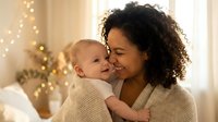 African American mother holding infant baby during Christmas season with warm bokeh lights creating cozy holiday atmosphere for family celebrations.