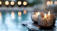 Glowing decorative candles in mosaic holders create peaceful ambiance against blurred water surface with soft bokeh lights in background. Perfect for spa settings.