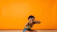 Young African American male athlete in dynamic stretching pose against vibrant orange background, wearing blue shorts and yellow top, suitable for fitness, wellness, and sports marketing materials.
