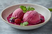 Pink raspberry ice cream scoops served in ceramic bowl with fresh berry sauce, mint leaves and fresh raspberries on gray background. Food photography.
