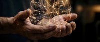 Elderly hands cupping glowing golden light sparks creating magical energy sphere against dark background for spiritual wellness concepts.