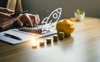 Business startup concept with hands using laptop, rocket icon, piggy bank and coin stacks representing financial growth and entrepreneurship planning.