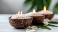 Aromatic coconut shell candles with sea salt and tropical palm leaves create serene spa atmosphere on white surface, natural wellness concept.