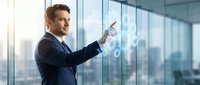 Professional businessman in dark suit interacting with futuristic holographic interface in modern office with large windows and city view background.