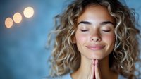 Young woman with curly blonde hair praying with closed eyes and gentle smile against blue background with bokeh lights, expressing peace and spirituality.