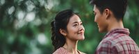 Young Asian couple sharing intimate moment outdoors with soft natural lighting and blurred green foliage background for romantic lifestyle content.