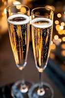 Two elegant champagne flutes filled with sparkling wine against warm golden bokeh lights background for celebration and festive occasions.