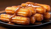 Freshly baked glazed French eclairs filled with cream and topped with caramel sauce arranged on dark plate, close up view of traditional pastries.
