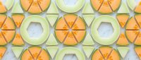 Colorful melon slices arranged in a geometric seamless pattern on a marble surface, tiles into a single background for summer food design.