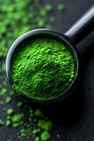 Vibrant green matcha tea powder in black measuring spoon on dark background, macro shot highlighting fine powder texture and intense natural color.
