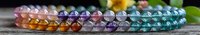Colorful crystal beads arranged in rainbow gradient pattern on rustic wooden surface, natural healing stones bracelet with soft bokeh background.