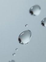 Floating water drops in macro photography against light gray background, showcasing surface tension and liquid dynamics in minimalist composition.