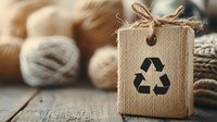 Eco-friendly gift box with recycling symbol and natural twine bow on rustic wooden surface surrounded by organic yarn skeins for sustainable packaging.