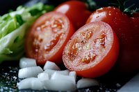 Fresh sliced tomatoes with diced onions and lettuce on dark surface for cooking and meal preparation.