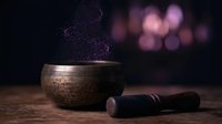 Tibetan singing bowl with purple glitter smoke and mallet on wooden surface with bokeh lights background for meditation and sound healing practices.