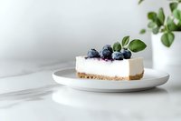 Fresh blueberry cheesecake slice on white plate against light background, garnished with berries and mint leaves, minimal food photography styling.