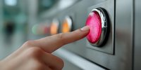 Finger pressing illuminated red emergency stop button on industrial control panel, safety concept for workplace hazard prevention.