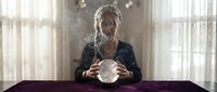 Elderly African American woman fortune teller with crystal ball at table in mystical room with floating cards and ethereal lighting atmosphere.