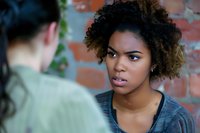 Young African American woman with natural curly hair expressing concern while listening intently during serious conversation against brick wall background.