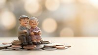Elderly couple figurines sitting on coins representing retirement savings and financial planning for senior years with warm bokeh background.