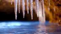 Sharp icicles hanging over frozen water surface with warm golden light creating dramatic winter atmosphere for seasonal designs and cold weather concepts.
